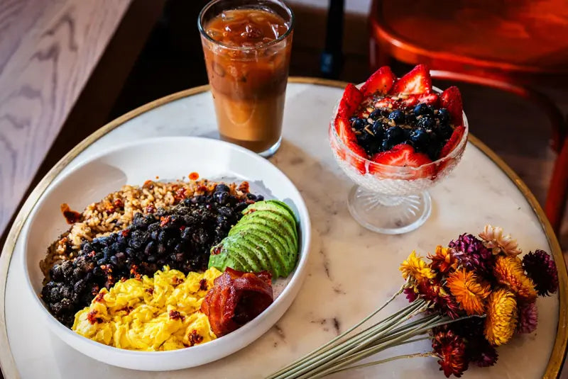 A breakfast bowl, fresh fruit, and iced coffee on a LeTish café table